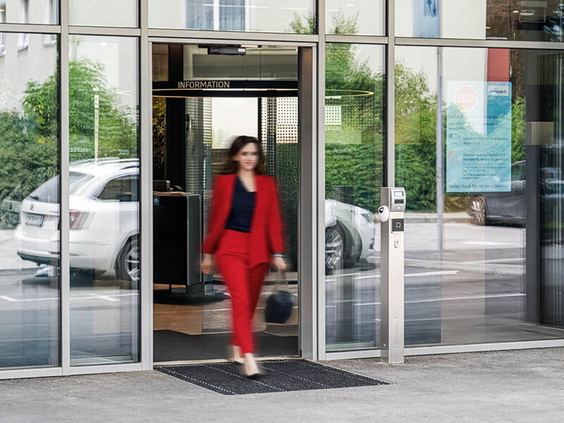 Ein Frau im roten Kostüm geht durch eine automatische Schiebetüre